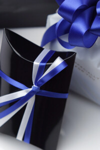 光沢のある黒の枕型箱に入れて青と白のシルクサテンリボンをかけます。さらに箱を上品な白の袋に収め、開いた花びらの形に結んだ青と銀のリボンをかけます。袋は水色の薄羽紙をふんわり敷いた白の外箱に入れてお送りいたします。箱を開けると清楚で凛とした美しさが広がります。